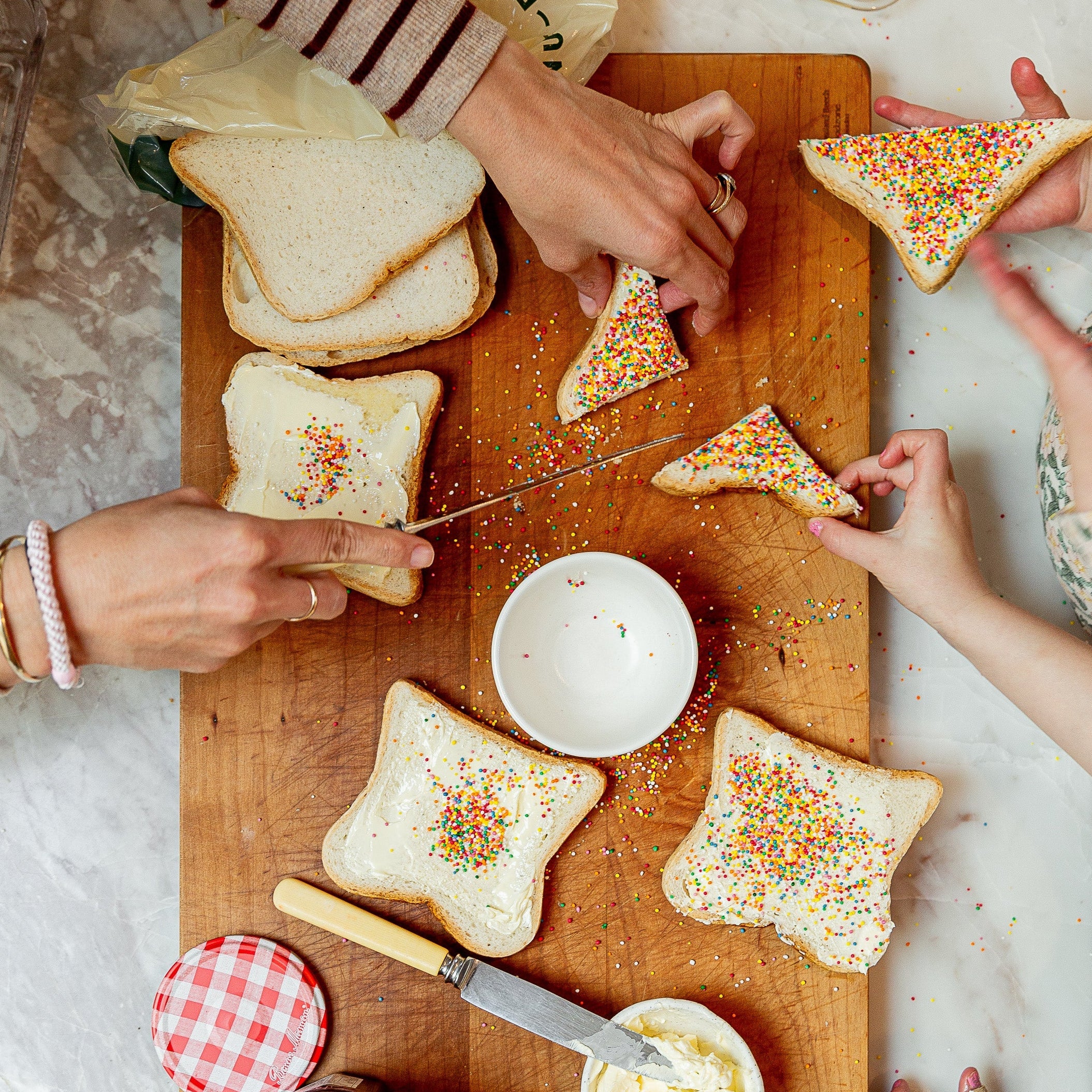 Kids making fairy bread on white bread with sprinkles and butter.
